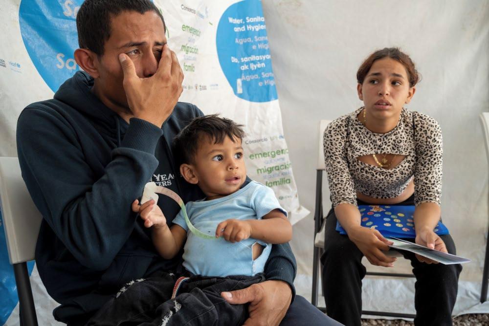 Hombre llorando con su bebé y otra hija en un centro de descanso para migrantes en Honduras - Acción contra el Hambre