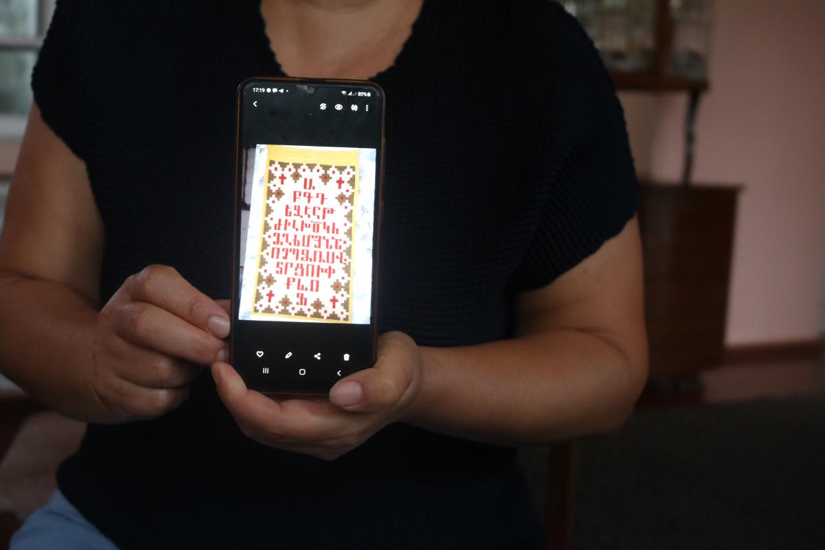 Nazik showing on her phone the kind of carpets, this one with the Armenian alphabet embroidered, that she was making in Nagorno Karabakh © Laurence Moureh for Action Against Hunger.