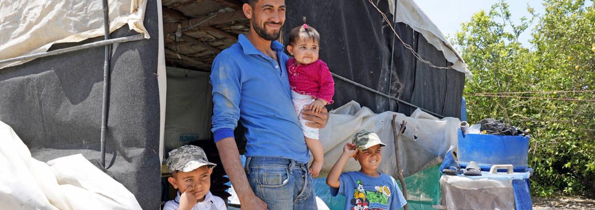 Un padre refugiado sirio posa frente a su tienda en el sur del Líbano con sus tres hijos.